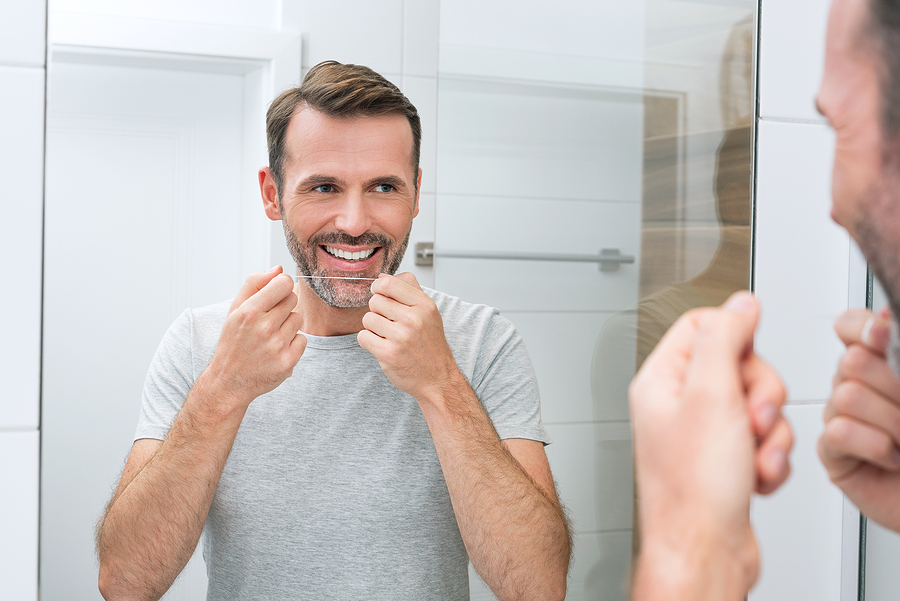 Man Using Dental Floss In The Bathroom. White Teeth And A Beauti